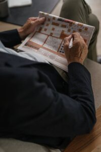 Un adulte âgé résolvant des mots croisés dans un journal, filmé à l'intérieur.