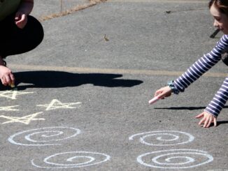 a young girl is drawing on the ground with chalk