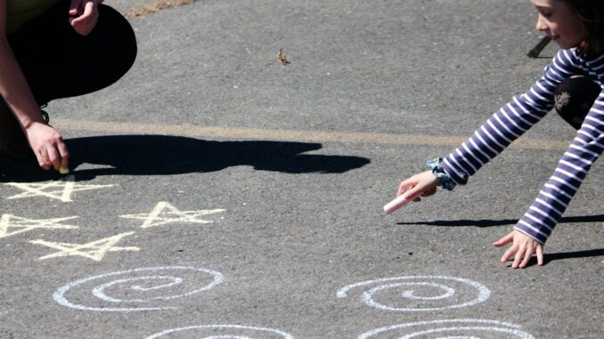 Photo by Danielle-Claude Bélanger a young girl is drawing on the ground with chalk