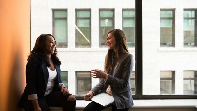 two woman sitting by the window laughing