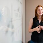 smiling woman presenting at whiteboard