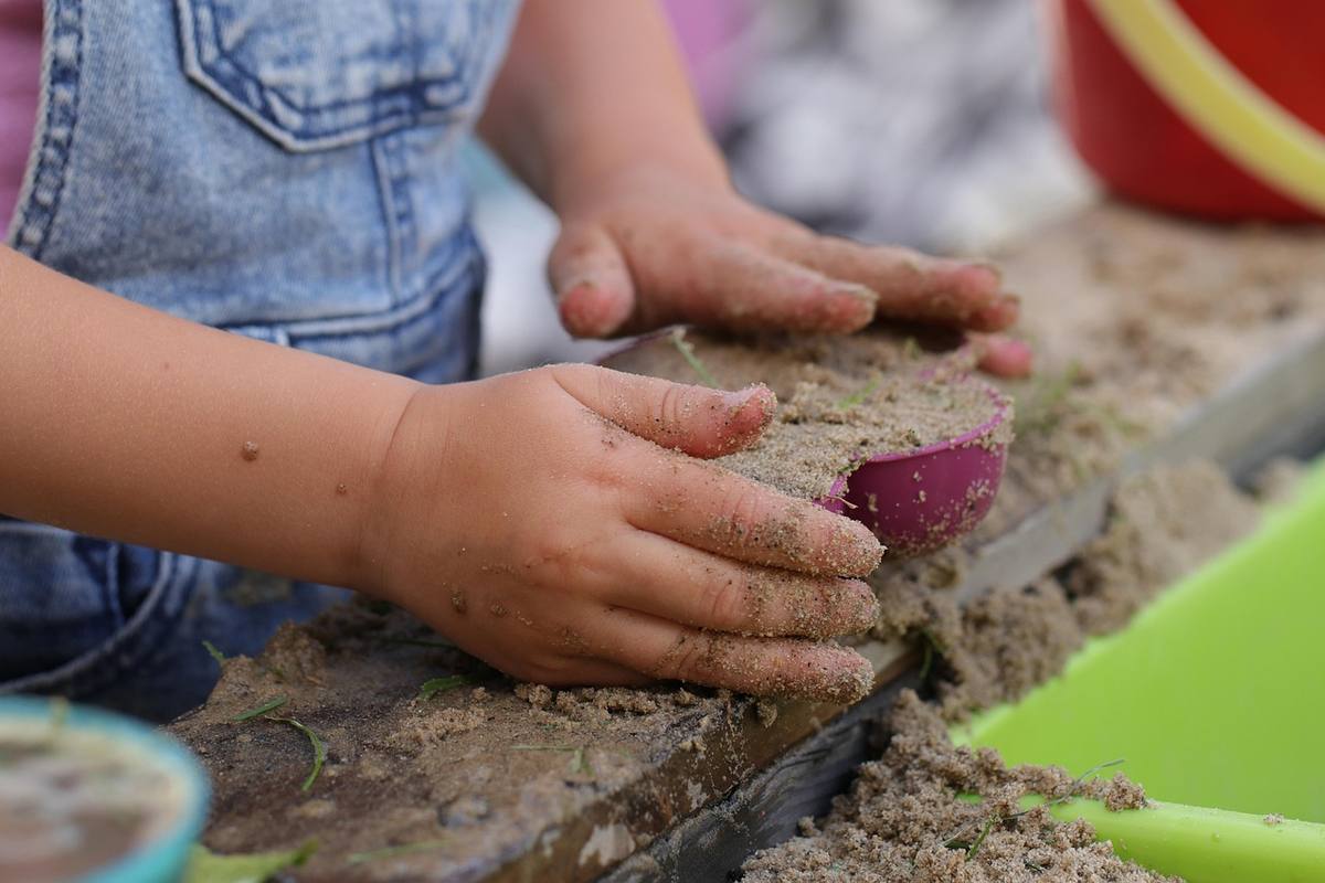 Mains d'enfant couvrées de sable, modelant une forme sur du gravier