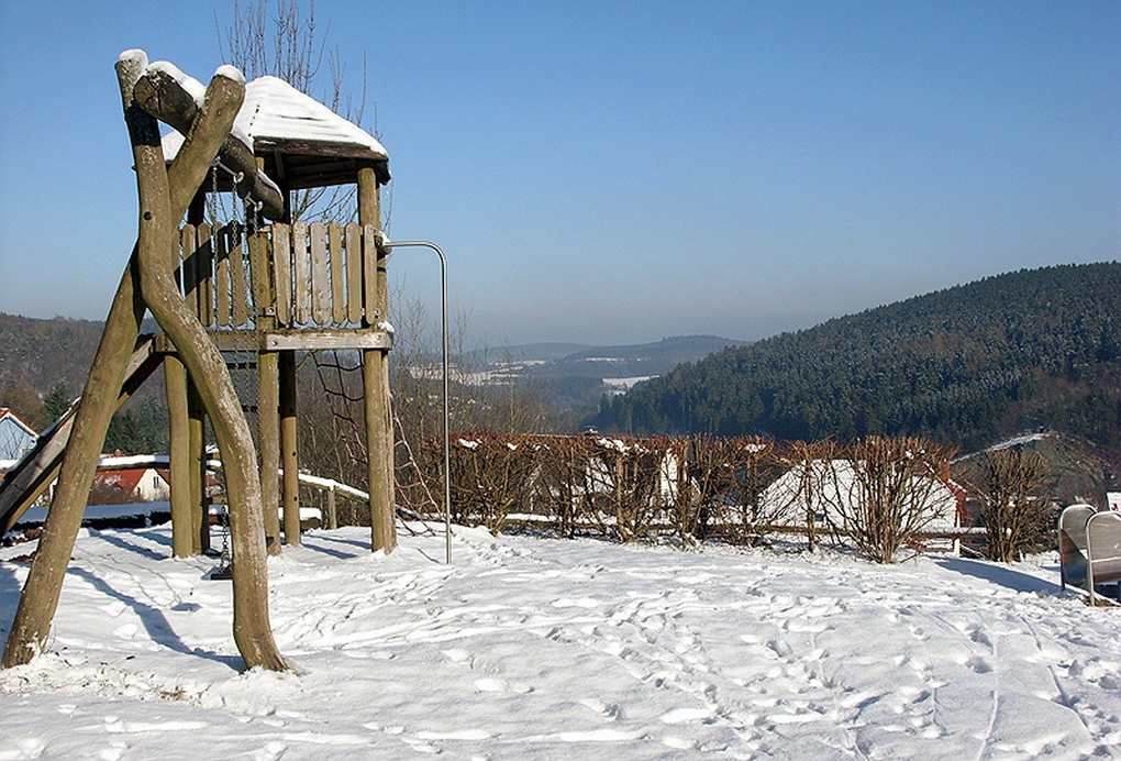 Structure de jeu en bois sur neige, avec toboggan et balançoire, vue panoramique sur des collines Structure de jeu en bois sur neige, avec toboggan et balançoire, vue panoramique sur des collines
