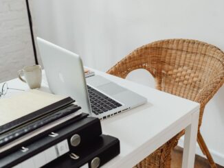 Un bureau avec ordinateur portable, tasse, dossiers et chaise en rotin