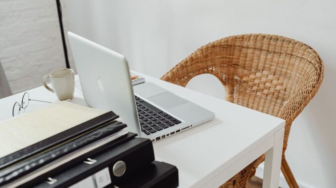 Un bureau avec ordinateur portable, tasse, dossiers et chaise en rotin